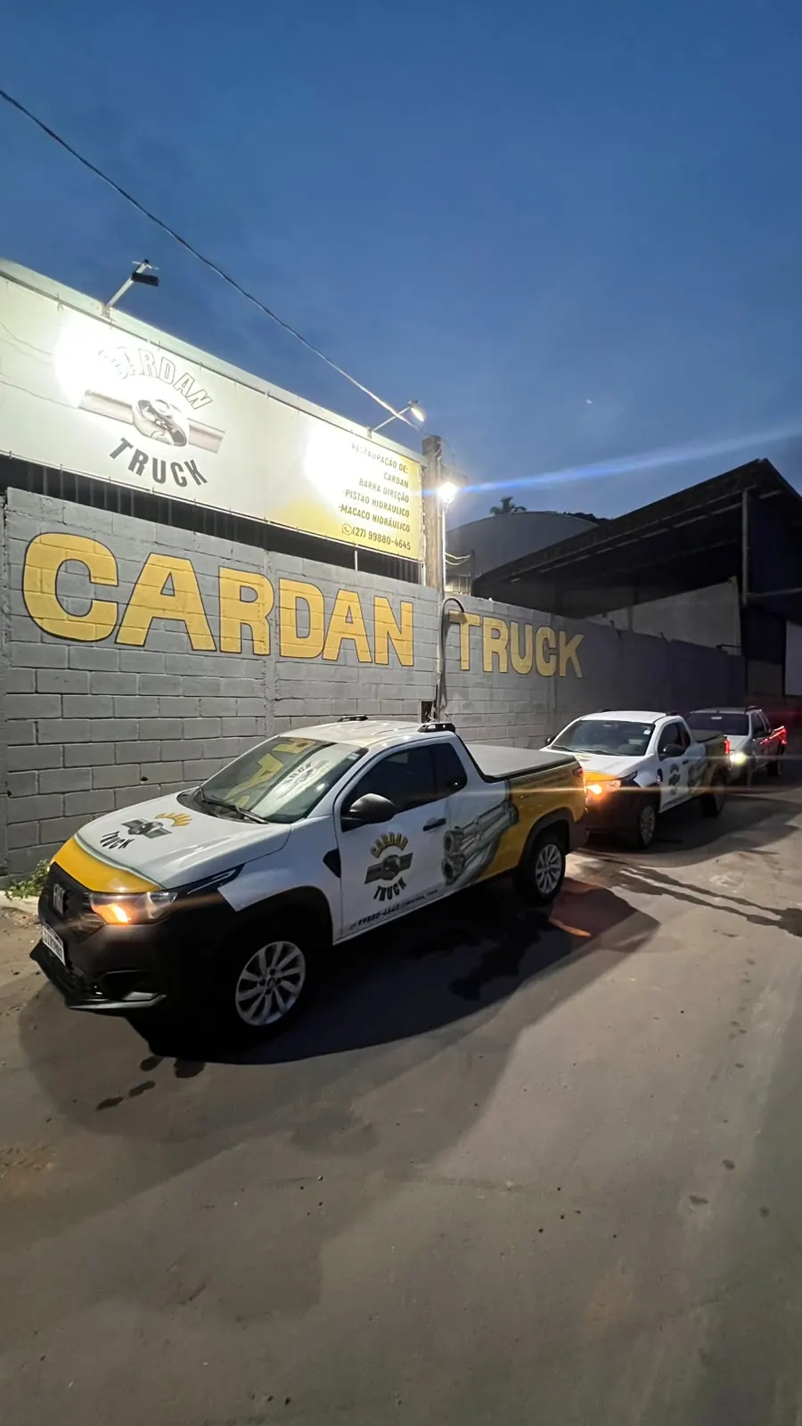 Frota de caminhonetes Cardan Truck estacionadas em frente à oficina ao entardecer